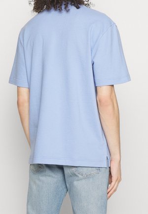 Helles blaues, kurzärmliges T-Shirt aus weichem Stoff, mit lockerer Passform und Seitenschlitzen am Saum, von hinten gezeigt.