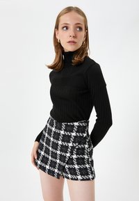 Czarny sweter prążkowany z długimi rękawami, zestawiony z czarno-białą mini spódnicą w kratę, która ma fakturę i wyraźny krój.