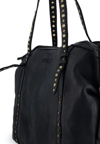 Černá kožená kabelka s kultivovanými zlatými hroty podél popruhů, strukturovaným tvarem a viditelným šitím. Značka je embosována na přední straně.