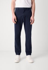 Marineblauwe chino's van lichtgewicht stof, met een rechte pasvorm, knoopsluiting en zijzakken. Gemaakt in combinatie met witte sneakers.