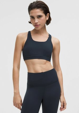 Czarny sportowy biustonosz wykonany z elastycznej tkaniny, z dekoltem typu scoop i szerokimi ramionami, w komplecie z pasującymi legginsami z wysokim stanem.