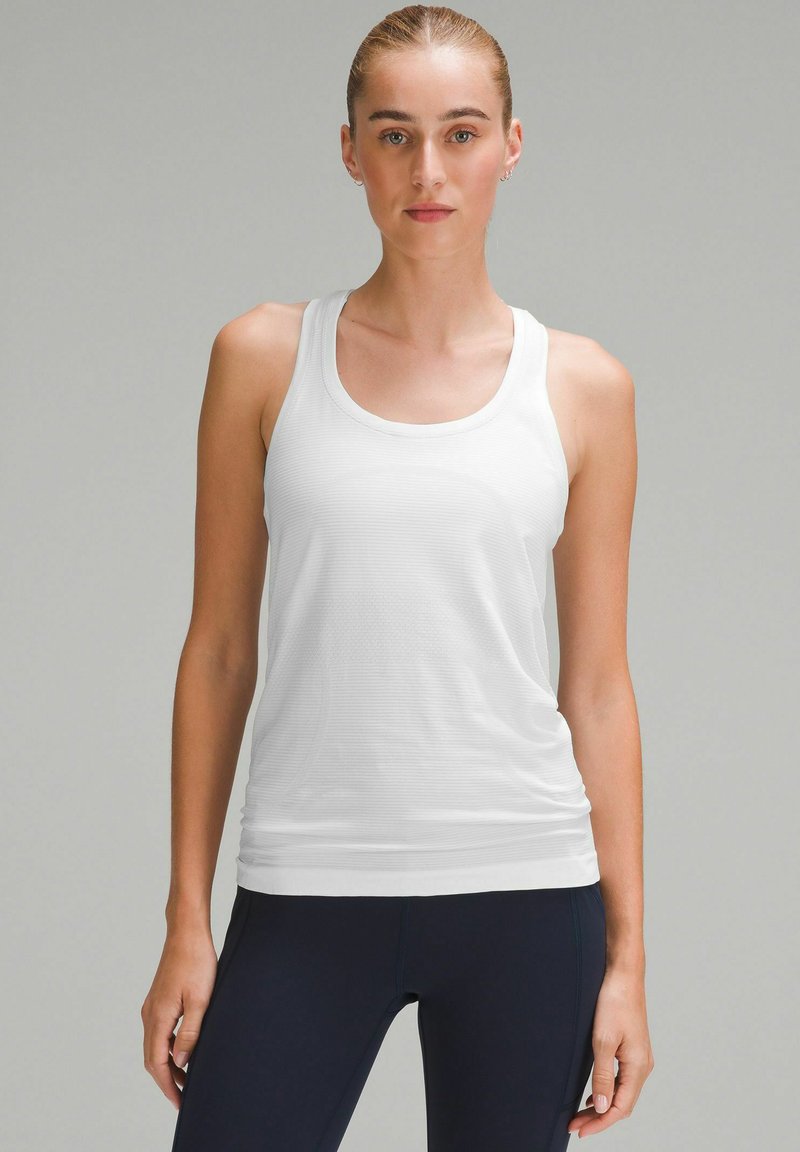 Débardeur de sport blanc avec un col arrondi, une texture côtelée et une coupe ajustée. Associé à des leggings bleu marine foncé pour un contraste.