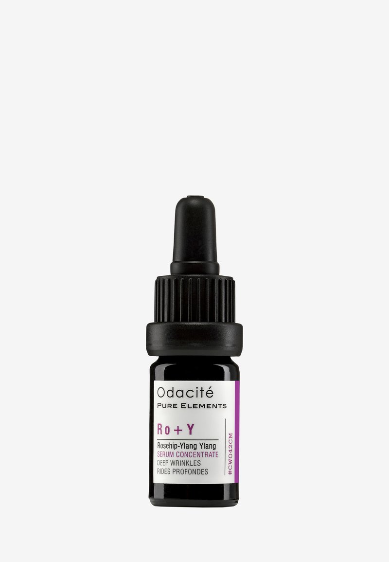 Odacité Rō + Y Ylang Ylang-serum i en svart glasdroppflaska. Har ett ribbat svart lock och en vit etikett med lila accenter.