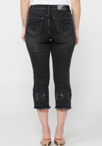 Crne traperice capri s izvezenim cvjetnim detaljima na poderanom rubu. Sadrži dva stražnja džepa s dekorativnim šavovima i oznaku loga.