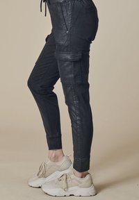 Schwarze Cargo-Jogginghosen aus glattem Kunstleder mit Seitentaschen, schmal zulaufenden Beinen und elastischen Bündchen. Kombiniert mit hellfarbigen Sportschuhen.