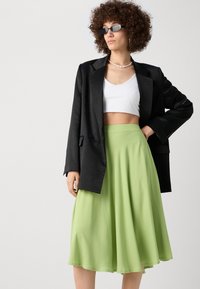 Svart blazer, hvit kort topp og et strømmende, lysegrønt skjørt. Stoffet er glatt, med en mid-length lengde og en avslappet silhuett.