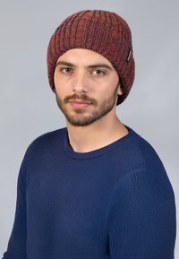Gehaakte beanie in een donkere oranje en blauwe mengeling, met verticale ribbels. Vergezeld van een textuurtrui in marineblauw, met ronde halslijn en aansluitende mouwen.