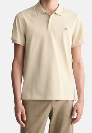 Polo beige en coton doux, doté d'une patte de boutonnage à trois boutons et de manches courtes. Comprend un logo discret sur la poitrine.
