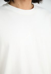 Witte katoenen t-shirt met een ronde halslijn en subtiele geborduurde Jordan-logo op de borst, met een zachte, gladde textuur.