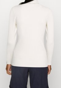 Långärmad, figurnära polotröja i ljusbeige ribbad tygkvalitet, med en mjuk textur och subtil sömdetaljering längs axlarna och nederkanten.