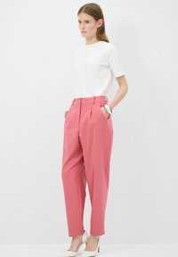 Witte t-shirt met korte mouwen, gecombineerd met hooggewijde roze broek met plooien en zijzakken. Het model draagt ook witte puntige hakken.