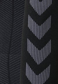 Czarna tekstylia z fakturowymi poziomymi paskami i pionowym wzorem w zygzak w odcieniu szarości. Miękka, gładka struktura; uniwersalny design odpowiedni do odzieży aktywnej.