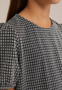 Topi kankaita yhdellä mustalla ja valkoisella ruutukuvioinnilla, lyhyillä puffihihnoilla ja pyöreällä pääntiellä, jossa on hienovarainen tekstuuri ja kiiltävät yksityiskohdat.