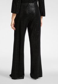 Czarne spodnie cekinowe o szerokich nogawkach, z fakturowaną powierzchnią i dopasowanym pasem. Rozszerzane od kolana w dół.