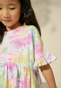Haljina s tie-dye uzorkom u pastelnim bojama ružičaste, zelene i žute, s širenim rukavima, naboranim rubom i mekim, laganim materijalom.