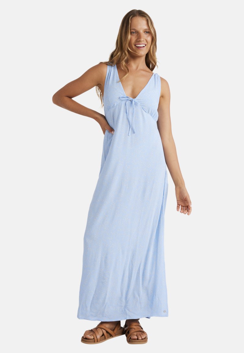Lichtblauwe maxi-jurk met een V-hals, strikdetail bij de borst en een zijsplit. Zachte stof met een subtiel patroon. Draag met bruine sandalen.