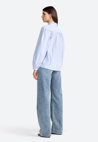 Blouse rayée bleu clair avec un col froncé, des manches longues et un détail froncé à l'arrière, associée à un jean en denim bleu clair à coupe ample.