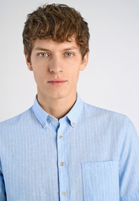Lichtblauw, knopenchemise met dunne witte verticale strepen. Bevat een borstzak en een standaard kraag. Katoenen textuur en een ontspannen pasvorm.