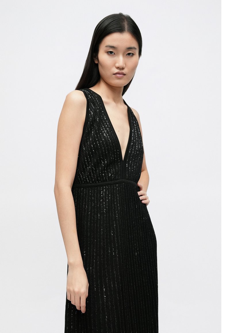 Black, sleeveless dress featuring a deep V-neck, vertical stripes, and textured fabric. The silhouette is fitted at the waist for a structured look.