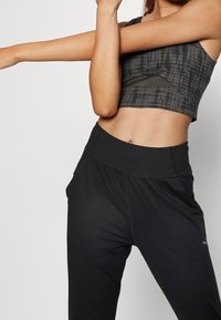 Czarny krótki top sportowy z teksturowanym szarym wzorem i siateczkowymi detalami, w połączeniu z czarnymi spodniami z wysokim stanem, z bocznymi kieszeniami.