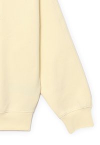 Felpa color crema con vestibilità morbida, maniche lunghe e polsini a coste. Realizzata in tessuto morbido e liscio con decorazioni minime.