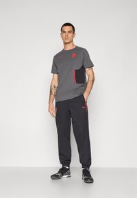 Grå atletisk T-shirt med sorte detaljer og lomme med rød lynlås, parret med sorte træningsbukser med røde detaljer og to cargo-lommer.