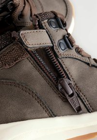 Braune Lederschuhe mit strukturiertem Finish, seitlichem Reißverschluss, dunklen Schnürsenkeln und Gummisohle. Akzente sind braune Nähte und Beschläge.