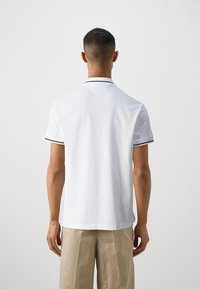 Camisa polo blanca de corte ajustado, con el cuello y los puños en negro en contraste, mangas cortas y una textura de algodón suave.