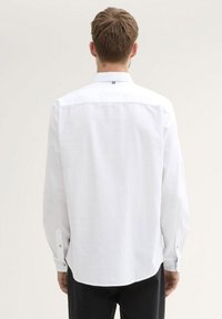 Witte langärmige shirt gemaakt van lichtgewicht stof. Heeft een klassieke kraag, knoopmanchetten en een gebogen zoom. Simpel ontwerp.