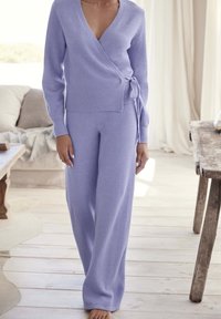 Lila gebreide trui met wikkelontwerp en strikdetail, gecombineerd met brede bijpassende broek. Zachte textuur, delicate v-hals, volwaardige mouwen.