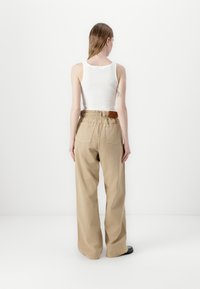 Hvit tanktopp og høy midje, løse lys beige bukser med elastisk midjebånd og to baklommer. Glatt stoff med minimalt med detaljer.