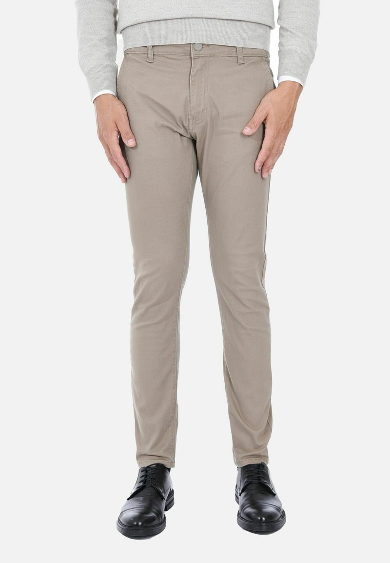 Pantaloni slim-fit beige in misto cotone, con zip e chiusura a bottone, e cinque tasche. Indossati con scarpe nere.