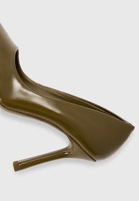 Escarpin vert olive à talon haut avec un bout pointu, fini en vernis brillant, silhouette élancée et un talon aiguille fin. Pas de matériel visible.