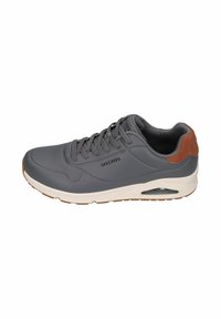 Zapatilla deportiva gris con una parte superior sintética suave, patrón perforado, acento en cuero de gamuza marrón en el talón y suela blanca con aire amortiguado.
