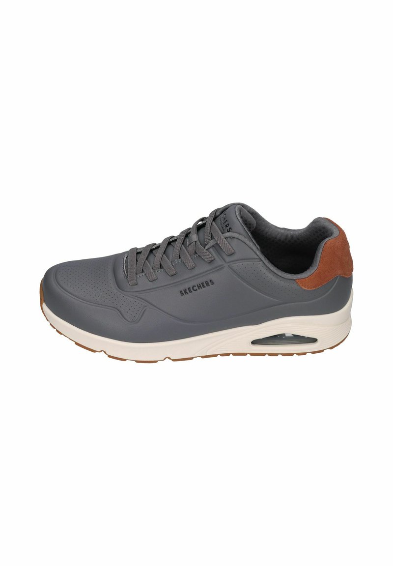 Zapatilla deportiva gris con una parte superior sintética suave, patrón perforado, acento en cuero de gamuza marrón en el talón y suela blanca con aire amortiguado.