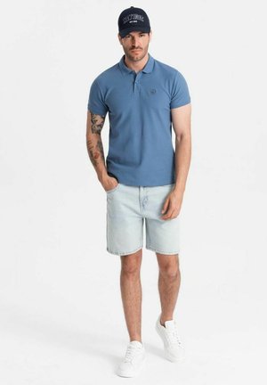 Blauwe polo met korte mouwen, lichtdenim shorts en witte sneakers. Pet voorzien van de tekst "New York". Eenvoudig ontwerp zonder patronen.