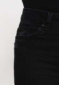 Jeans de mezclilla negra con un diseño ajustado, que cuentan con un bolsillo frontal, un suave desgastado y una cinturilla clásica con un botón de metal.