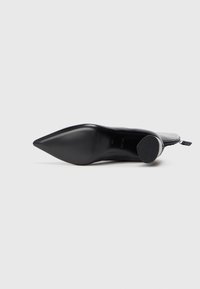 Zapato de tacón puntiagudo de cuero negro con una textura suave y un tacón afilado. Presenta una tapa de tacón redondeada y una silueta elegante.