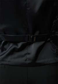 Giacca nera realizzata in un morbido materiale satinato. Dettaglio della cintura notevole con una fibbia metallica rettangolare, tessuto testurizzato e design strutturato.