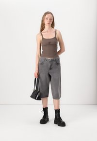 Brun ribbet tanktopp med tynne stropper, grå baggy denimshorts, svarte snørebøtter og en liten svart håndveske.