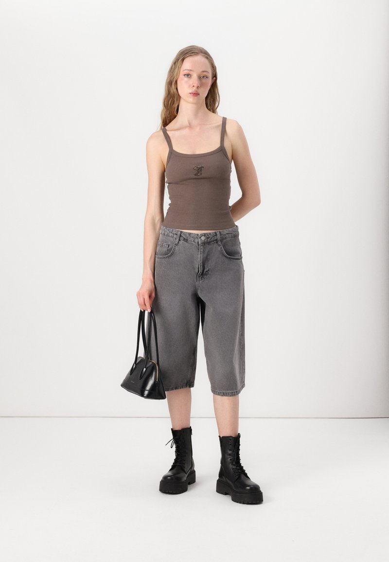 Brun ribbet tanktopp med tynne stropper, grå baggy denimshorts, svarte snørebøtter og en liten svart håndveske.