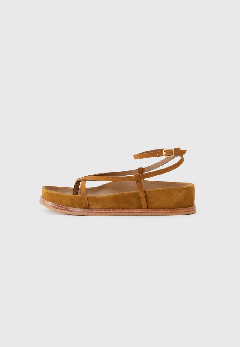 Brun mockaskandal med minimalistisch design, featuring tunna remmar och platt sula, som visar en naturlig textur och en rund form.