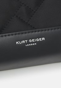 Czarna pikowana torba z nylonu z gładkim wykończeniem z czarnej skóry. Na froncie znajduje się srebrny tłoczony napis "Kurt Geiger London".