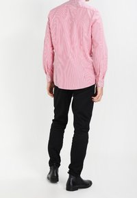 Maglietta a maniche lunghe a righe rosse e bianche con polsini a bottone, abbinata a pantaloni neri slim-fit e stivaletti neri alla caviglia. Collo semplice e dettaglio della spalla sul retro.