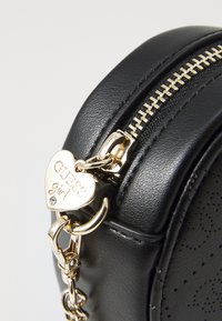 Borsa in faux leather nero con finitura testurizzata, zip dorata e charm a forma di cuore con incisa la scritta "GUESS girl". Forma rotonda, hardware lucido.