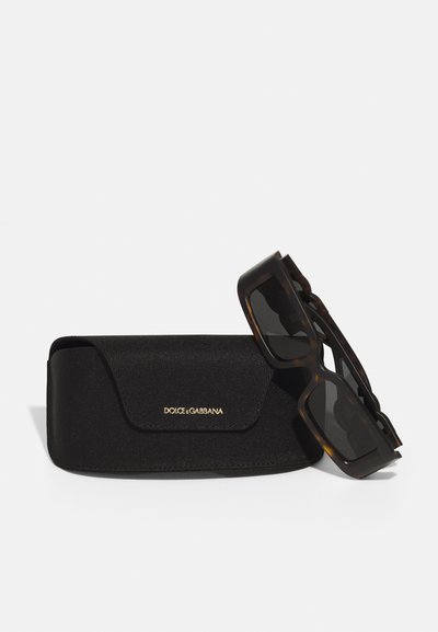 Ochelari de soare Dolce & Gabbana din tartă închisă, cu o carcasă texturată neagră ce prezintă un logo auriu. Design unghiular și lentile întunecate.