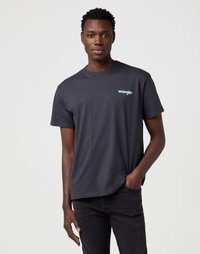Pel�ēka kokvilnas T-krekls ar īsām piedurknēm un apaļu dekoltē. Uz kreisā krūšu puses ir neliels zils "Wrangler" logo. Kombinēts ar melnajām džinsām.