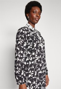 Black and white shirt with an elephant pattern, buttoned collar, and long sleeves. Made of smooth fabric with a relaxed fit.