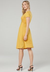 Senfgelbes knielanges Kleid mit tailliertem Oberteil, kurzen Ärmeln und einem ausgestellten Rock. Glatte Textur und dezente Raffung am Taillenbereich.