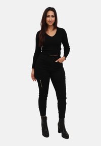 Zwart cropped trui met een V-hals, gecombineerd met zwarte cargobroeken met ritszakken, afgewerkt met zwarte platform enkellaarsjes.